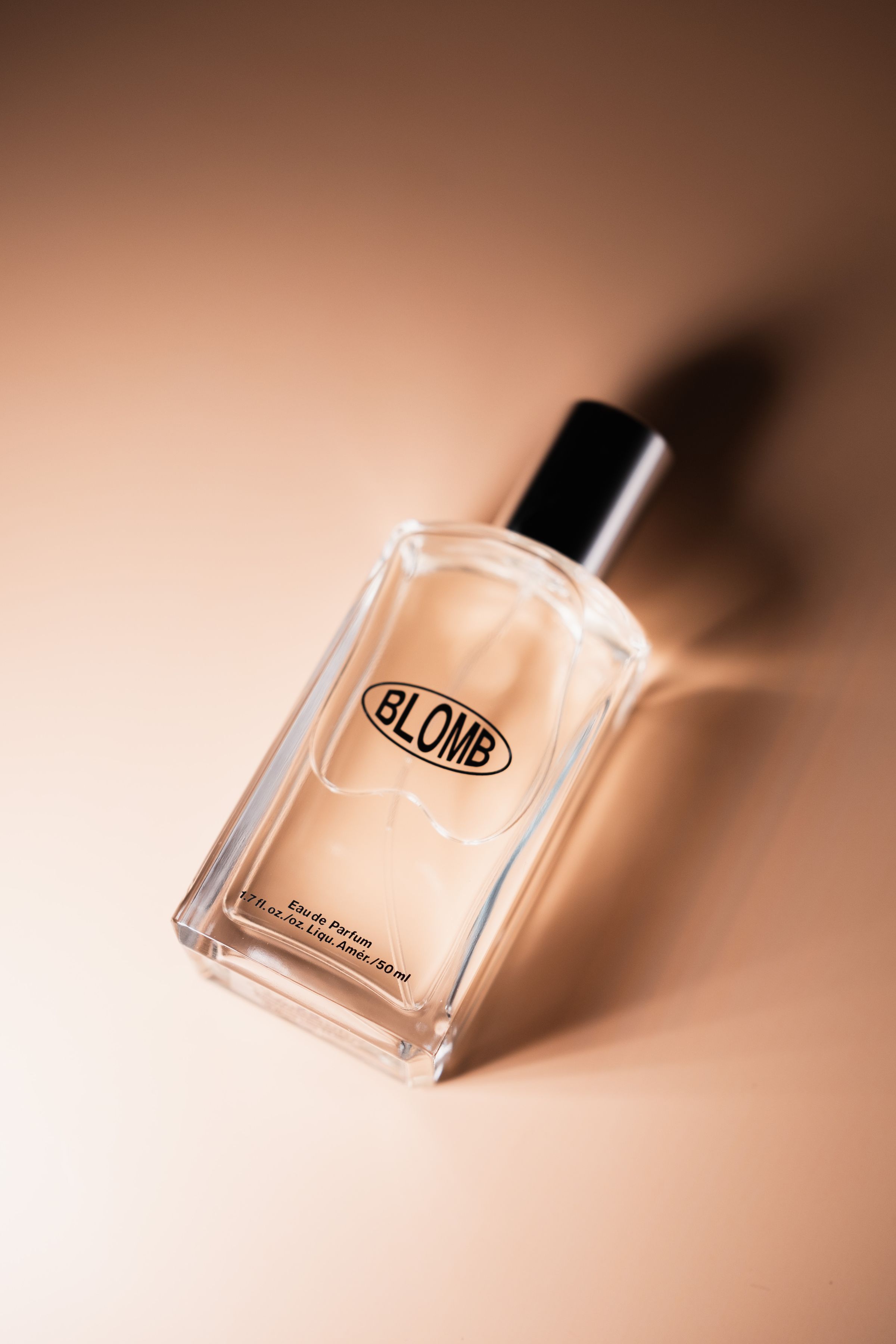 Glass perfume bottle with soft shadows on a warm neutral studio background