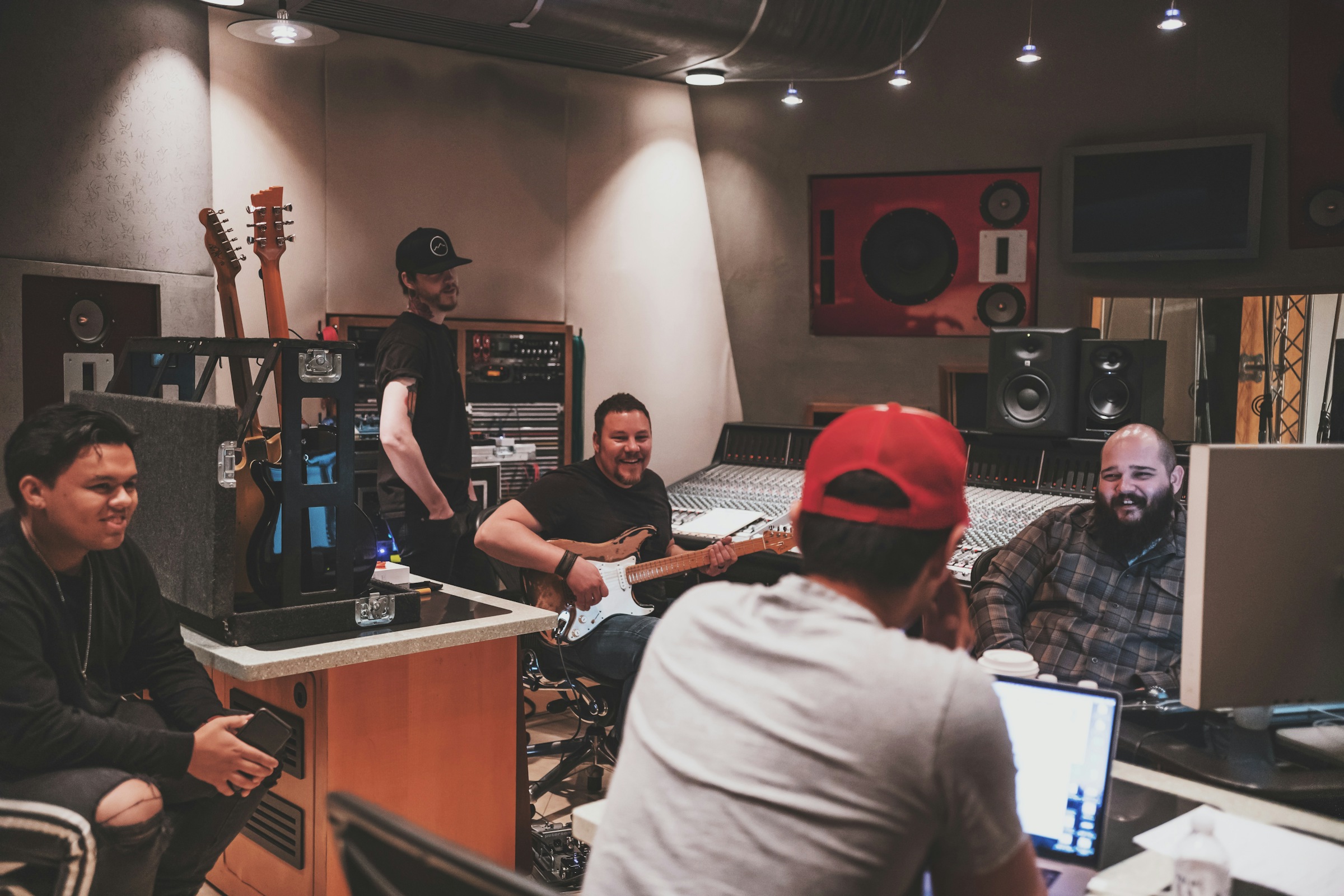 Creative team smiling and laughing around computers and a mixing desk in a recording studio